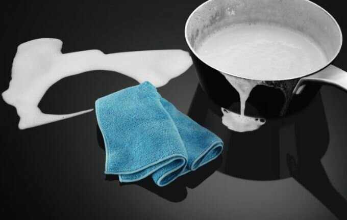 Niebieska szmatka i czarny garnek z mlekiem rozlanym na czarnym blacie.