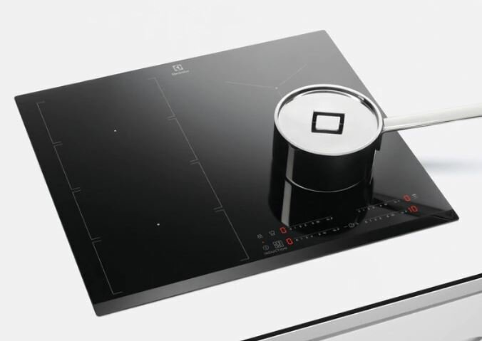 Czarna płyta indukcyjna z garnkiem. Płyta ma strefy gotowania i panel sterowania.