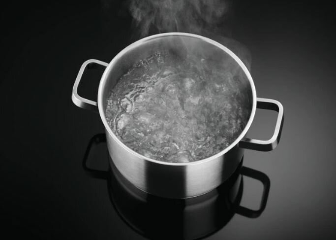 Garnek ze stali nierdzewnej z wrzącą wodą na czarnej płycie indukcyjnej.
