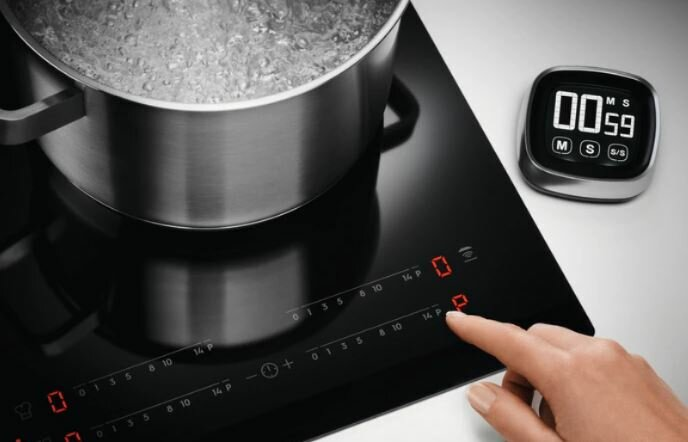 Czarny blat kuchenny z garnkiem wrzącej wody i timerem.