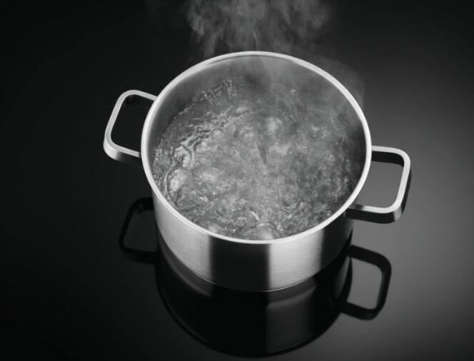 Garnek ze stali nierdzewnej z wrzącą wodą na czarnej płycie grzewczej.