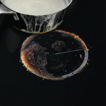 Czarna płyta grzewcza z przypalonymi resztkami jedzenia wokół palnika. Garnek kapie.