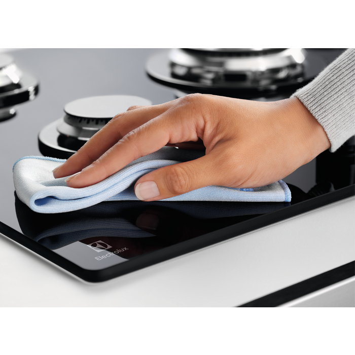 Ręka czyszcząca czarną płytę grzewczą niebieską szmatką, widoczne logo Electrolux.