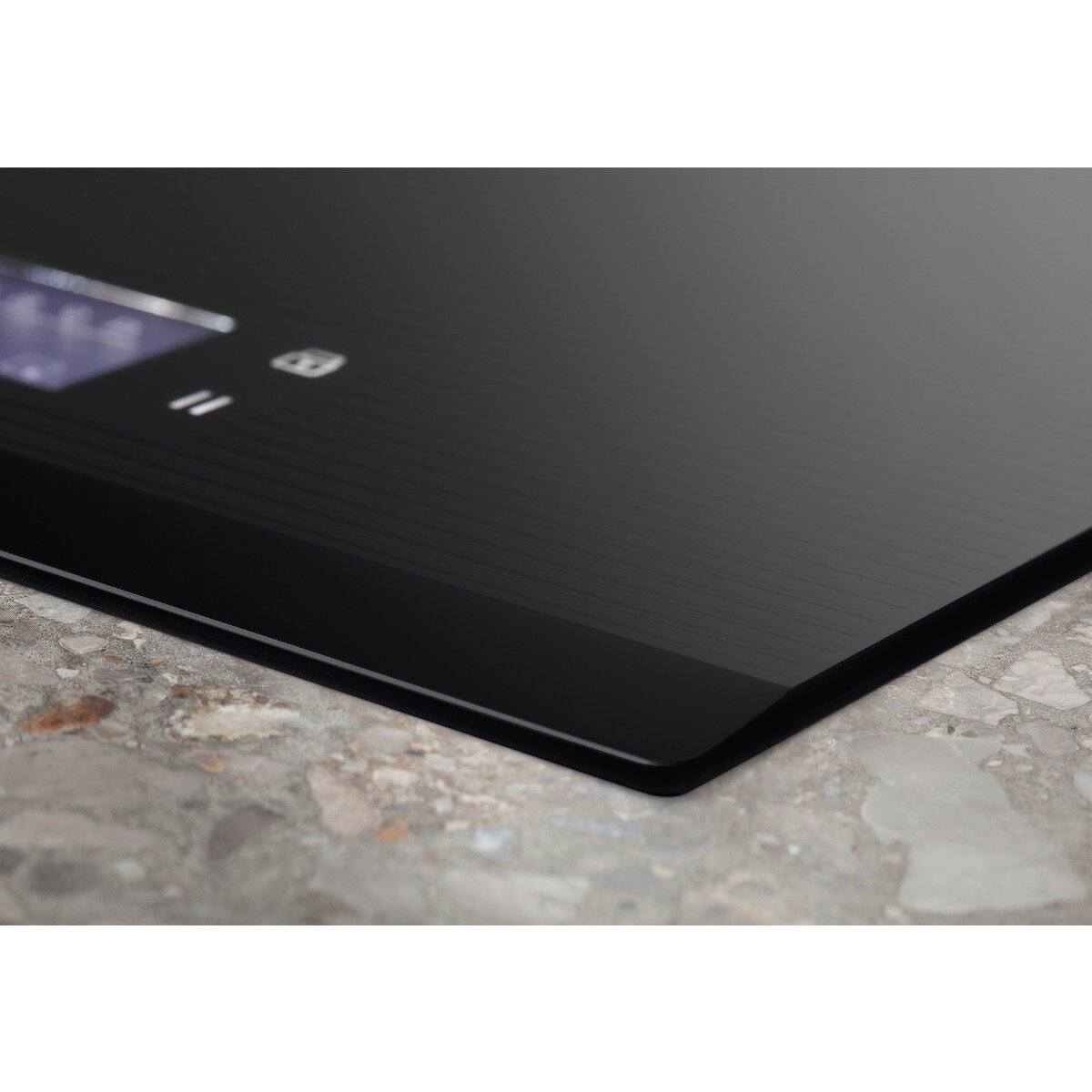 Zbliżenie czarnej płyty grzejnej z elementami sterowania dotykowego na szarej powierzchni.