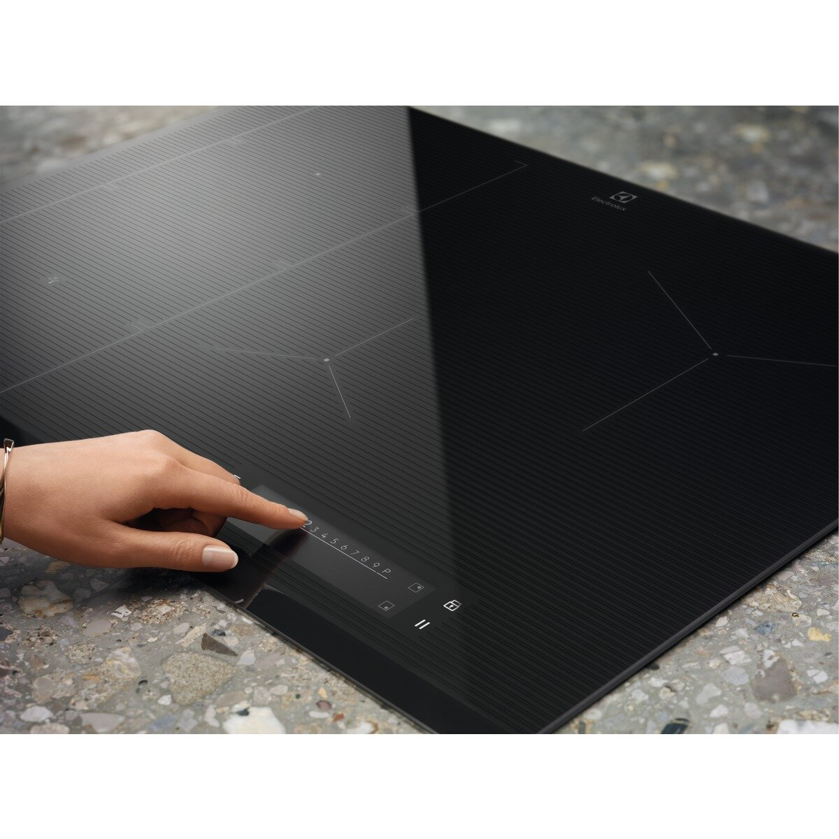 Zbliżenie na czarną płytę indukcyjną, dłoń dotyka panelu sterowania. Płyta stoi na kamiennym blacie.