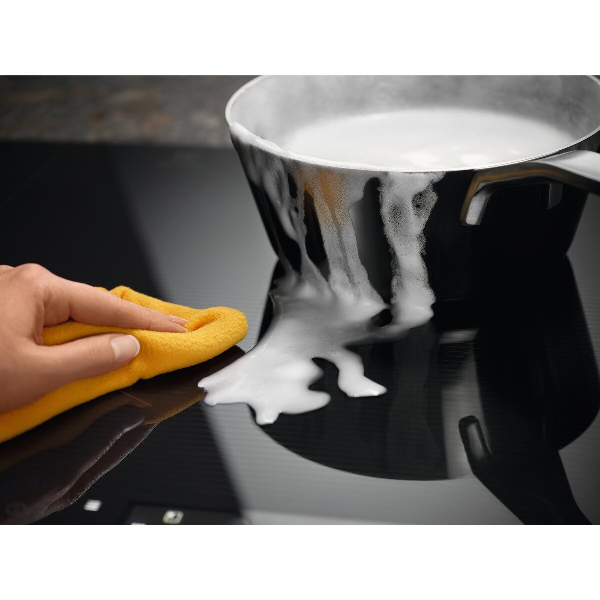 Żółta szmatka wyciera czarny garnek z pieniącą się pianą.