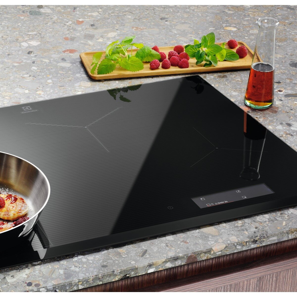 Czarna płyta indukcyjna z patelnią, malinami, miętą i fiolką.