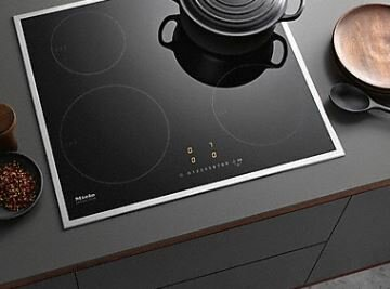 Czarna płyta grzewcza z czterema strefami gotowania. Garnek i drewniany talerz na wierzchu.