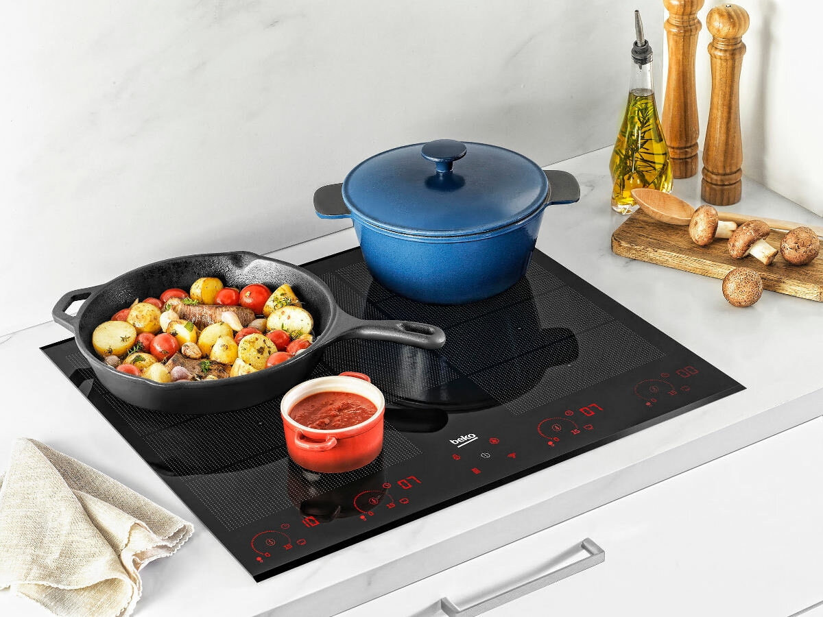 Płyta indukcyjna z garnkami i patelniami na niej, na białym tle.