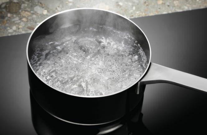 Czarny garnek na czarnej płycie kuchennej z wrzącą wodą, wytwarzającą parę.