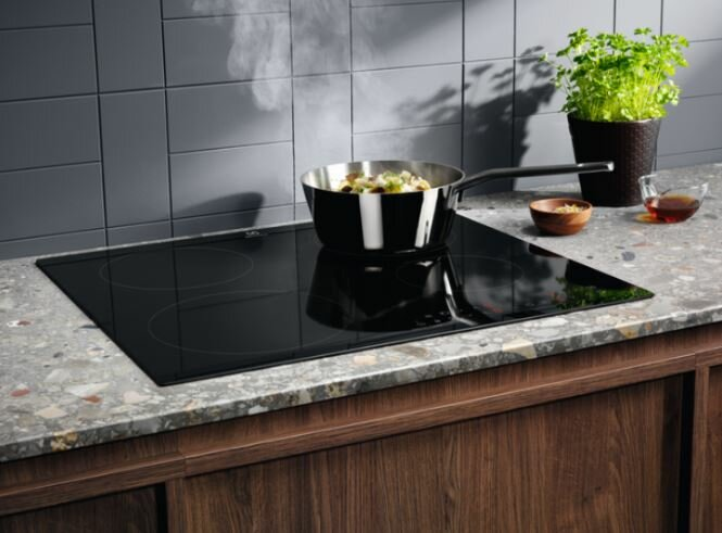 Czarna płyta grzewcza z patelnią gotującą jedzenie, roślinami i akcesoriami.