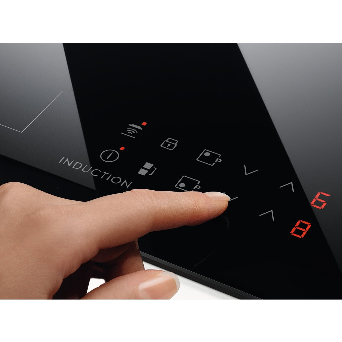 Dłoń dotykająca czarnego panelu sterowania płyty indukcyjnej z czerwonym wyświetlaczem.