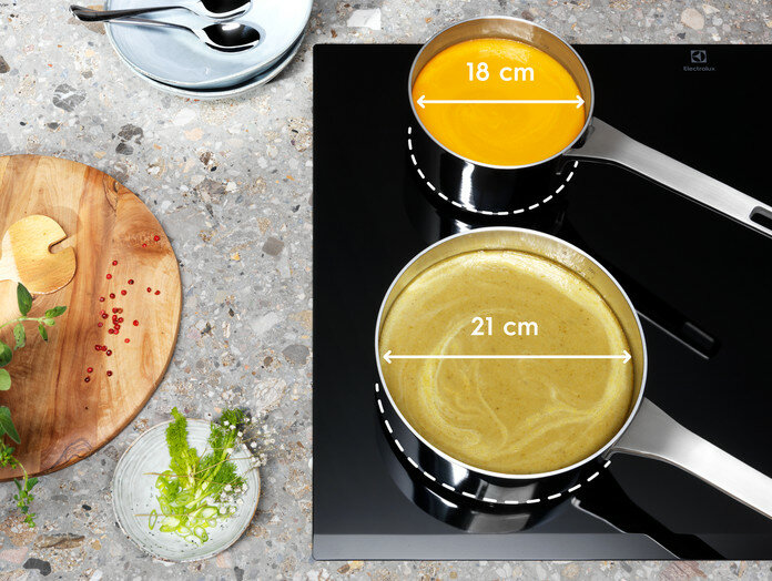 Dwa garnki na czarnej płycie indukcyjnej. Pomiary wskazują średnice 18cm i 21cm.