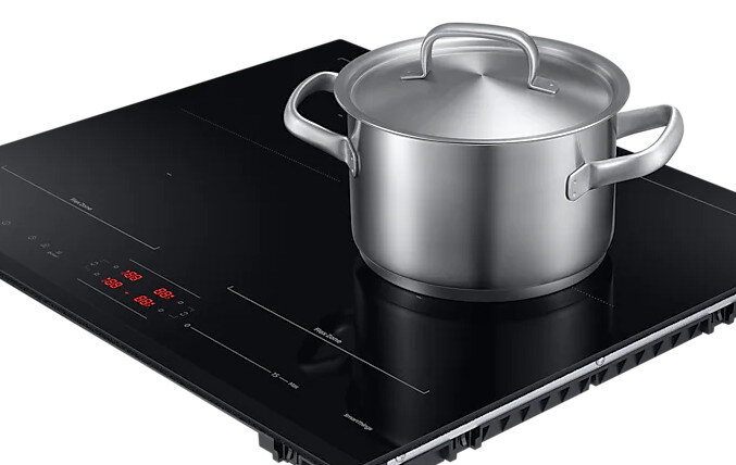 Czarna płyta indukcyjna ze srebrnym garnkiem na wierzchu. Czerwony wyświetlacz jest obecny.