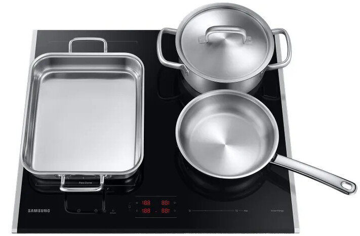 Czarna płyta grzejna ze stalowymi naczyniami: patelnią, garnkiem i prostokątną tacą.