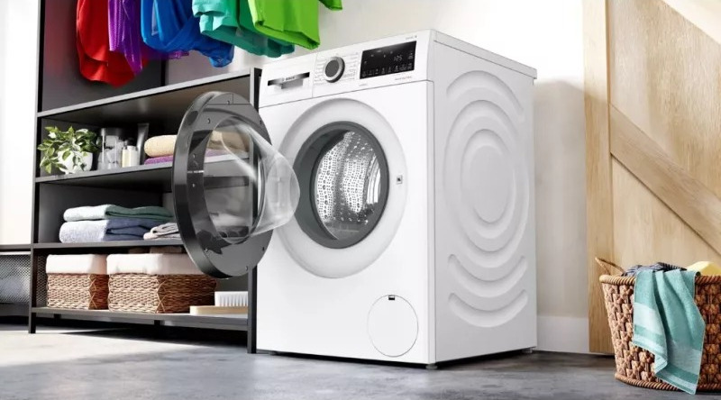 Witte wasmachine met een open deur, wasmanden en kleding.