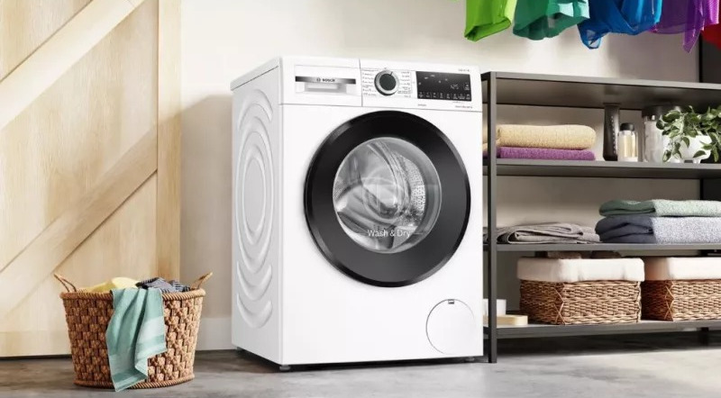 Witte wasmachine met een zwarte deur en een mand met groene doek ernaast.