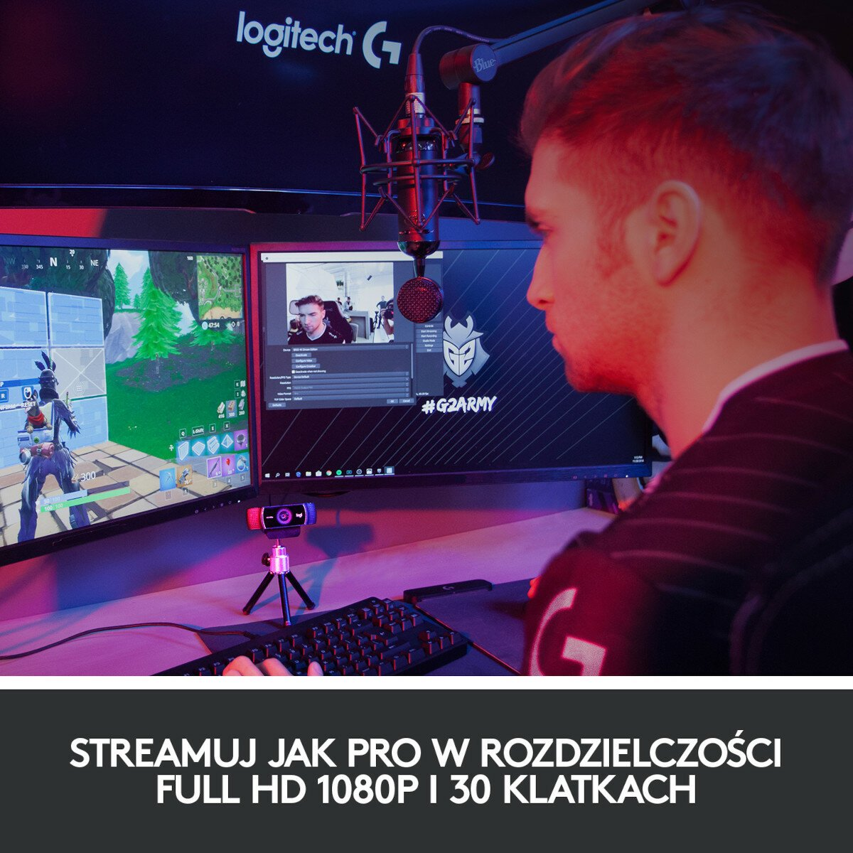 Gracz streamujący z dwoma monitorami i sprzętem, z logo G2Army na ekranie.