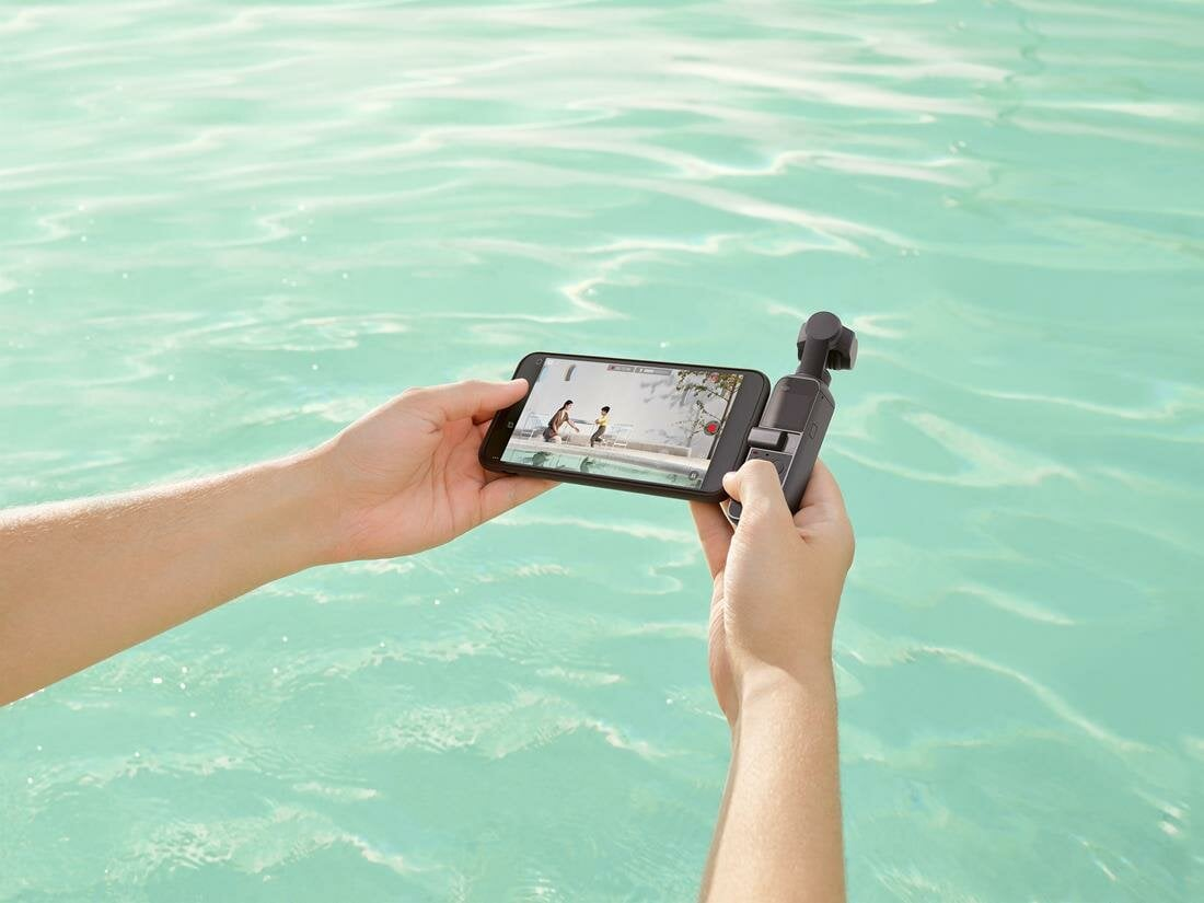 Osoba trzymająca telefon i mały stabilizator filmujący wodę.