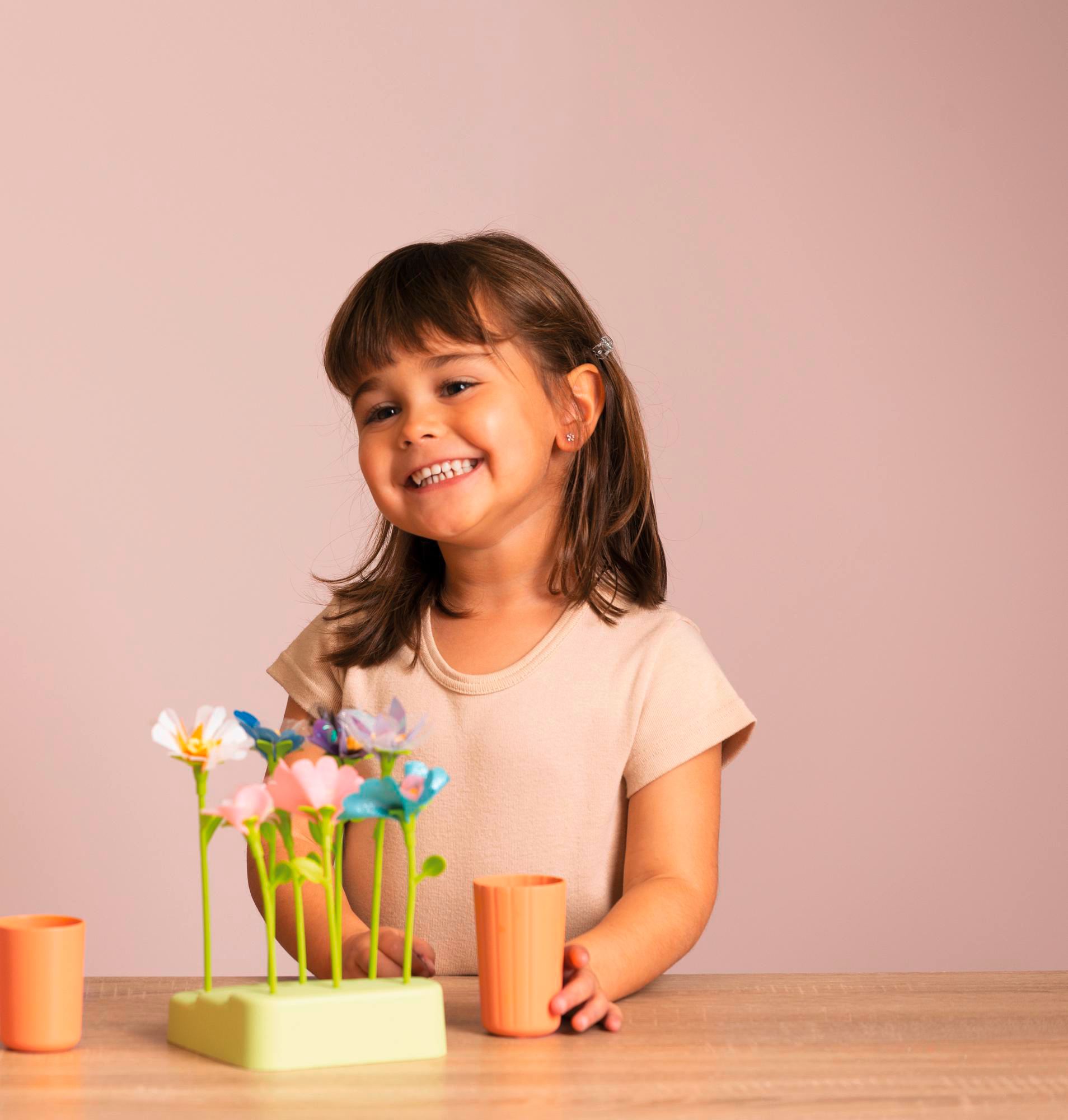 Ein lächelndes Kind mit einem Blumenspielzeug. Das Spielzeug steht auf einem Tisch.