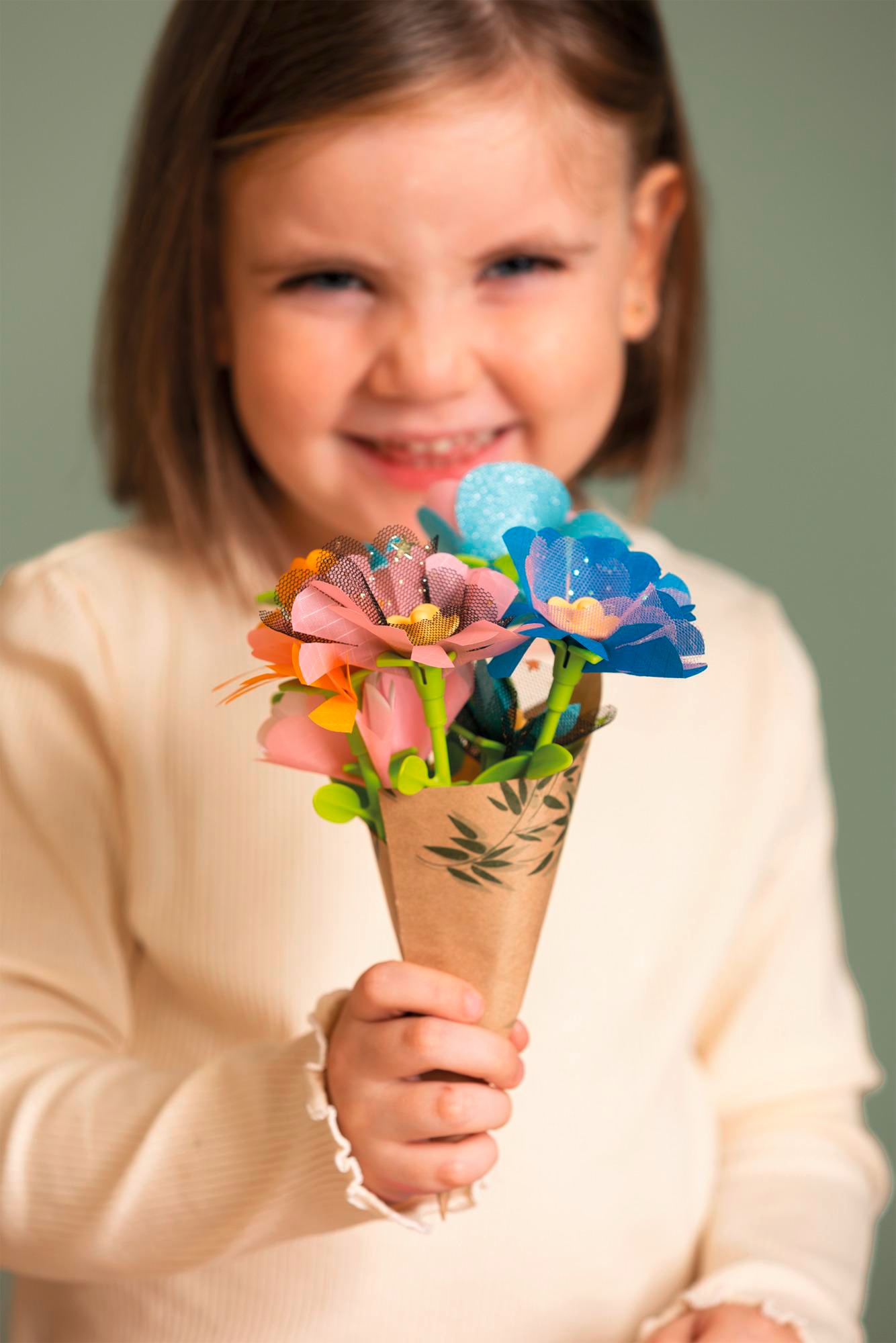Ein Mädchen hält einen Papierkegel mit bunten Kunstblumen. Sie lächelt, verschwommener Hintergrund.