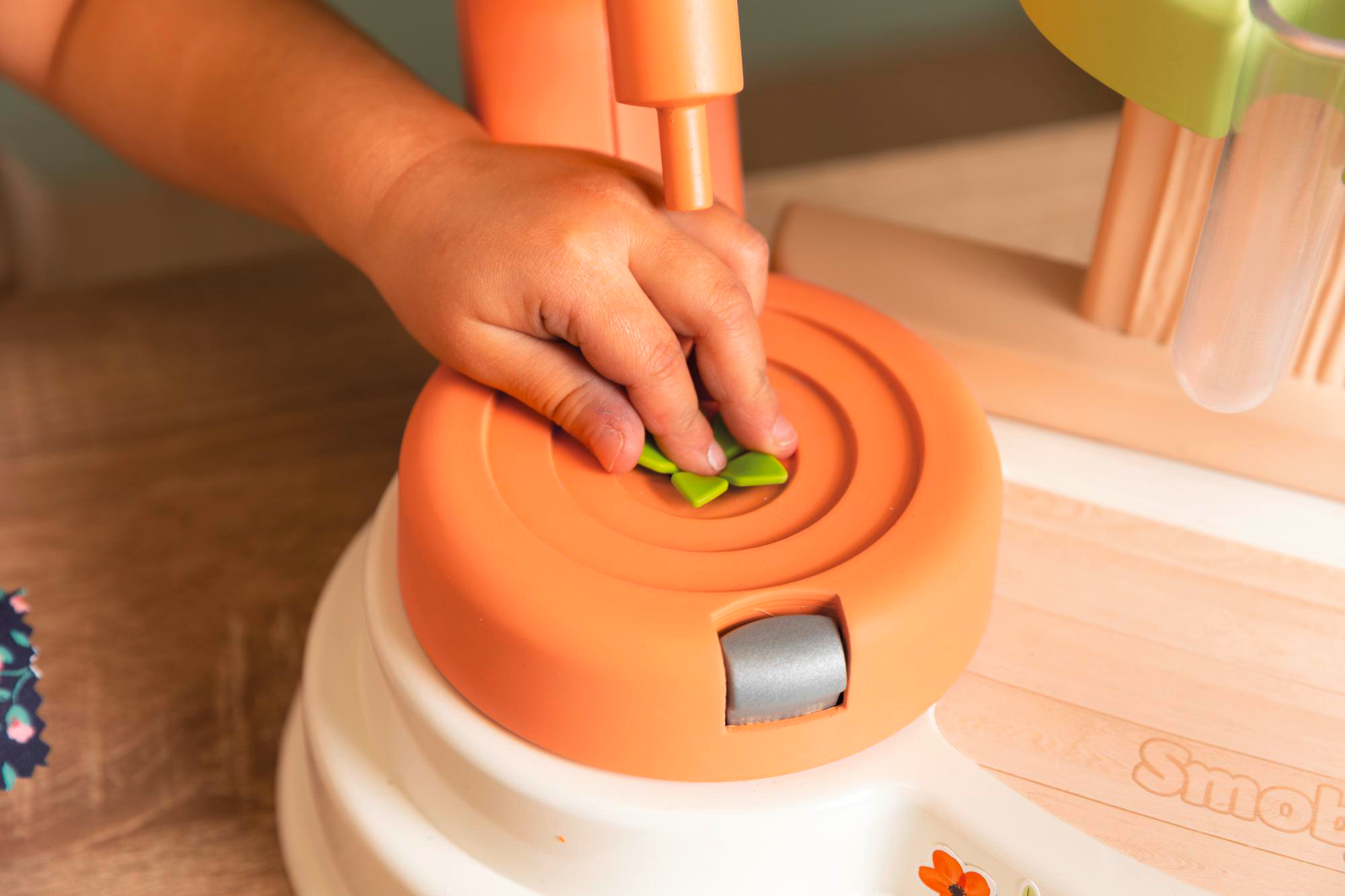 Kindeshand, die ein grünes Blatt auf ein oranges Spielzeug legt. Holzoberfläche.