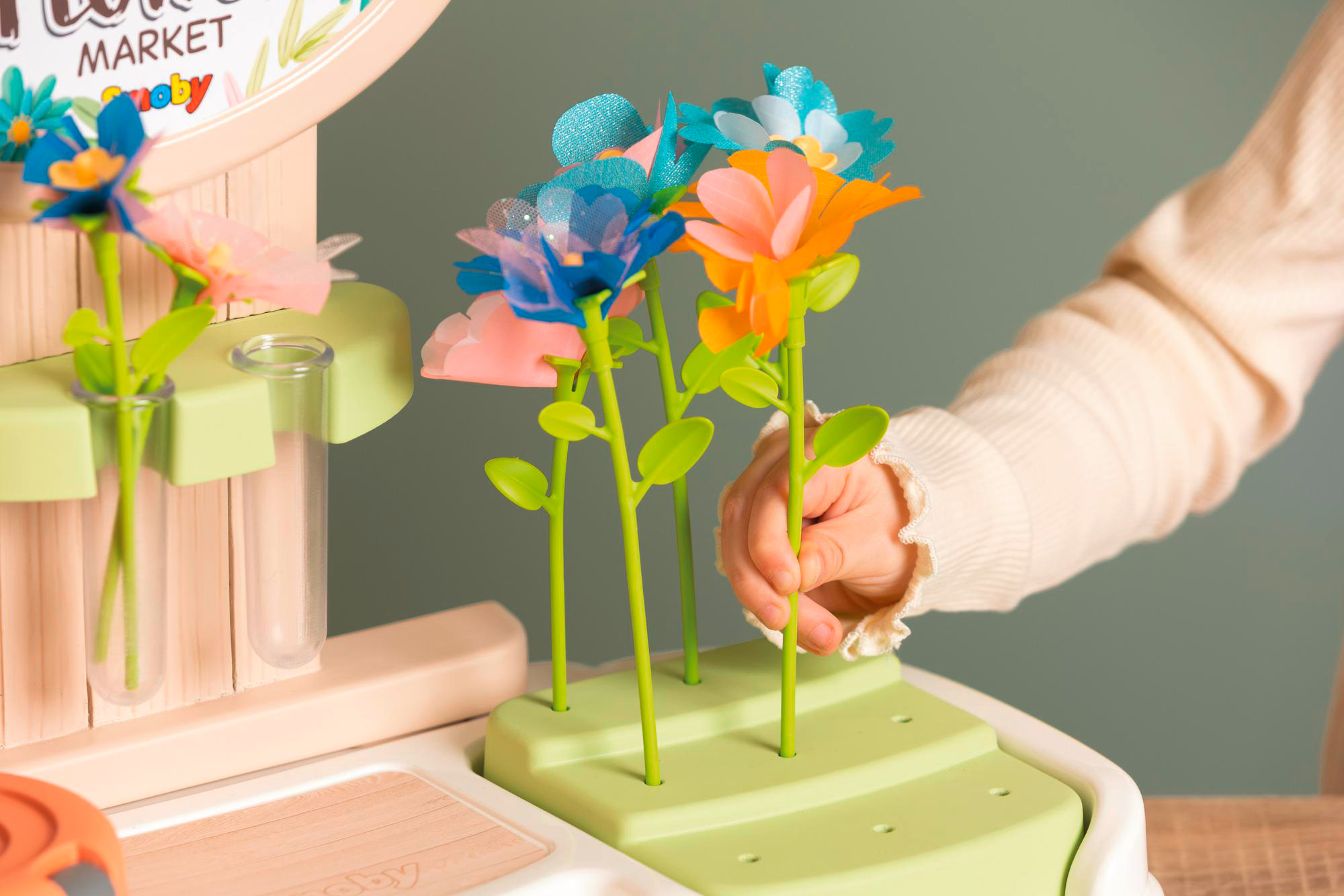 Hand des Kindes, bunte Papierblumen in grünem Gartenspielzeug anordnend.