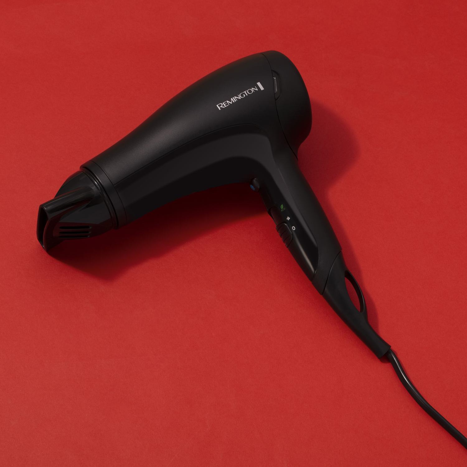 Zwarte haardroger op een rode ondergrond, met het merk Remington zichtbaar.