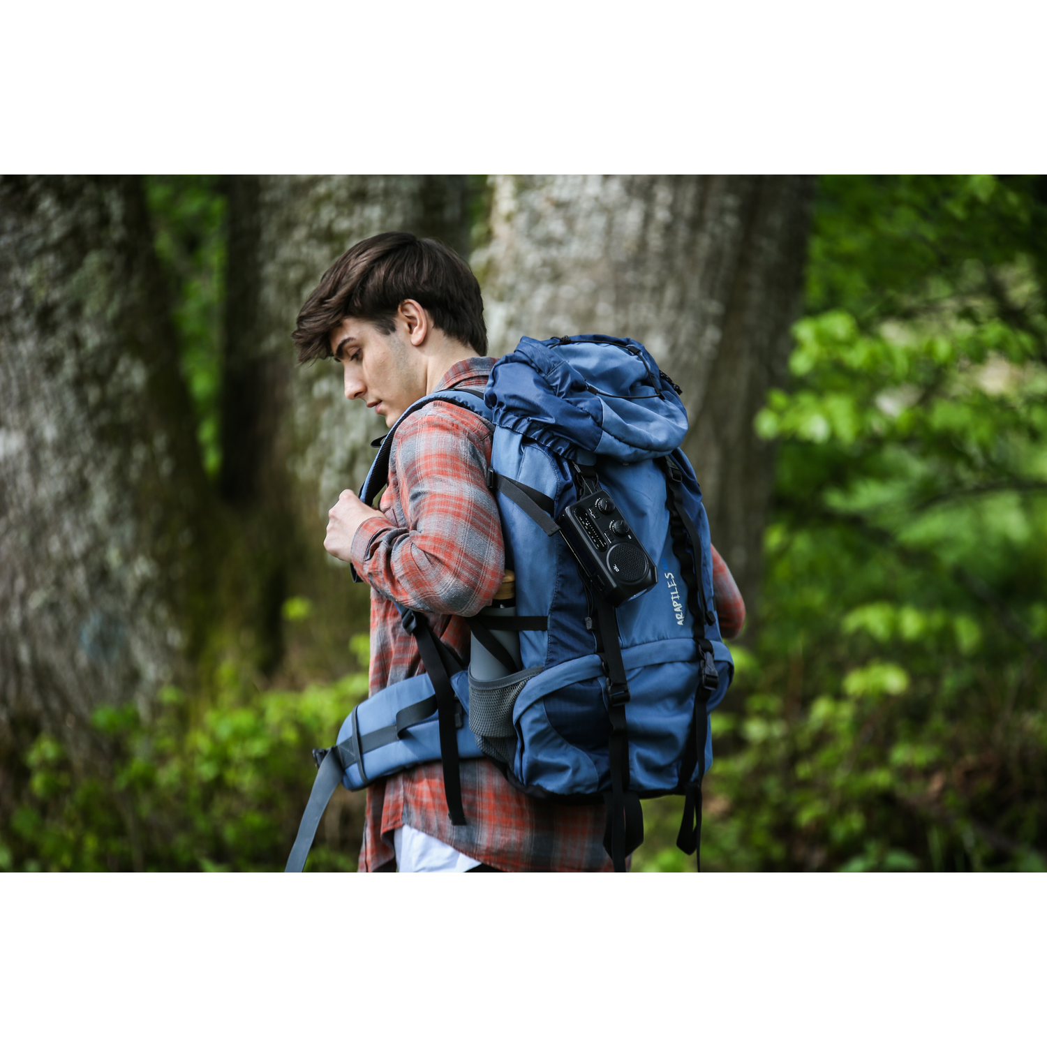 Man met rugzak die in het bos loopt. Rugzak is blauw, man draagt geruit overhemd.