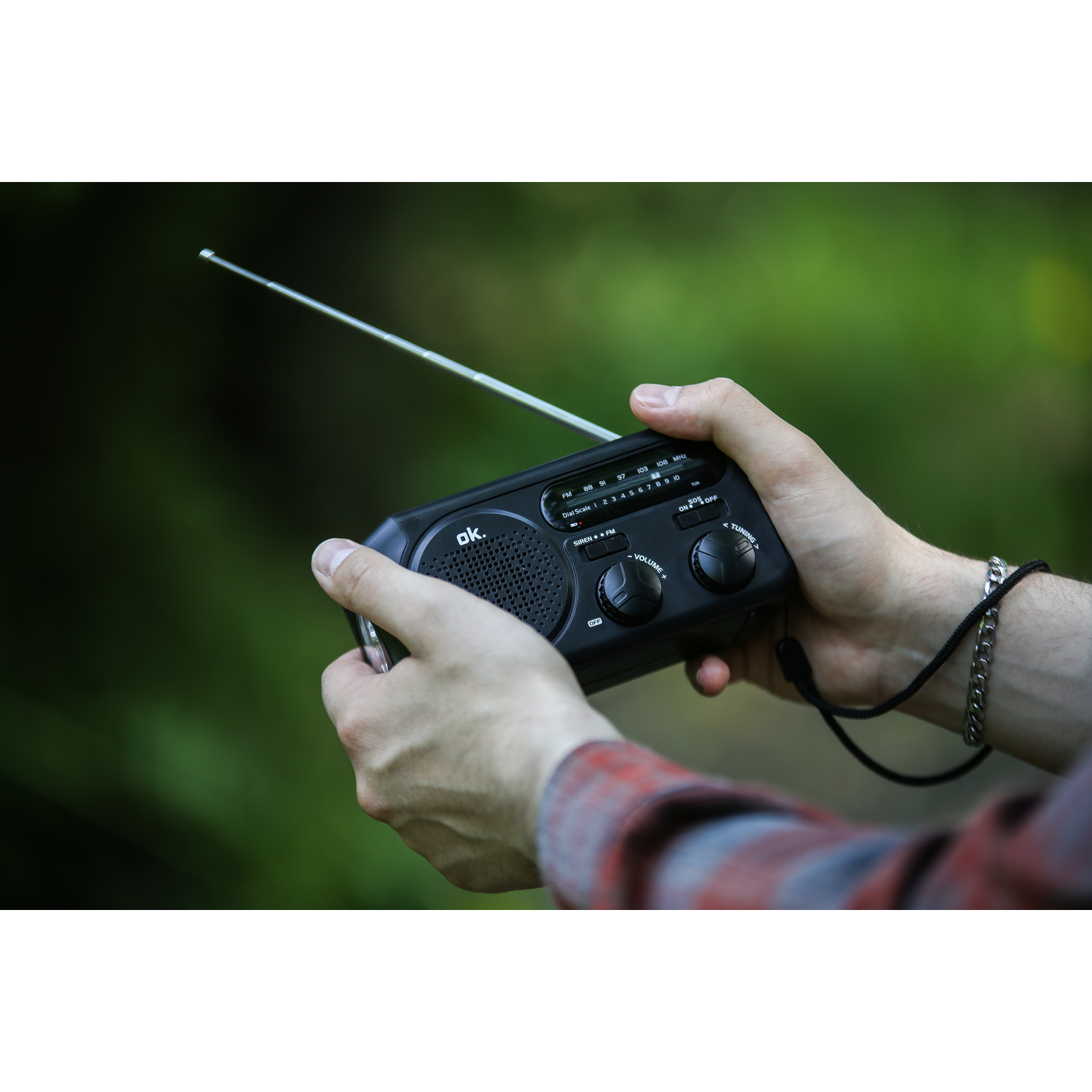 Handen die een zwarte radio vasthouden met uitgeschoven antenne, wazige groene achtergrond.