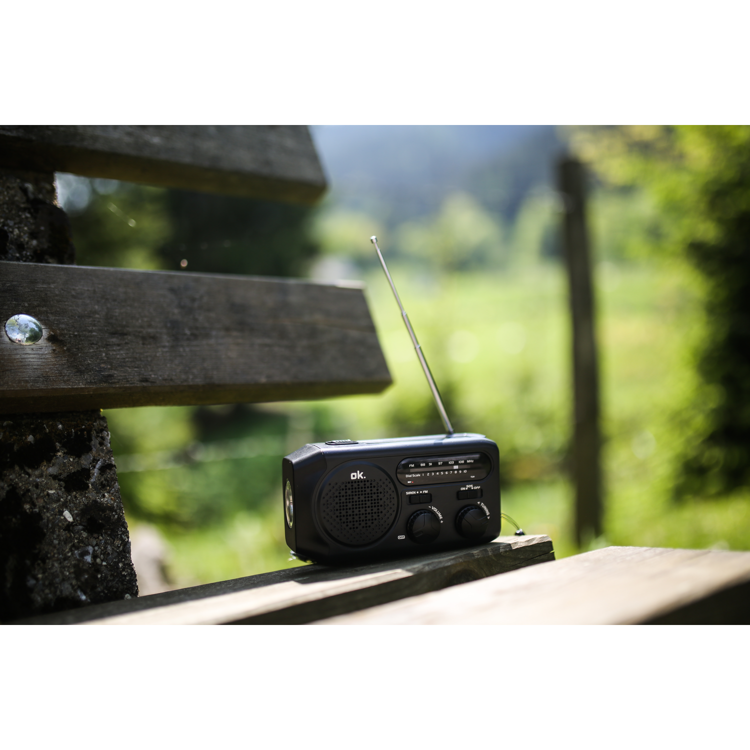 Zwarte radio op een houten bank, met een vage groene achtergrond van bomen en planten.