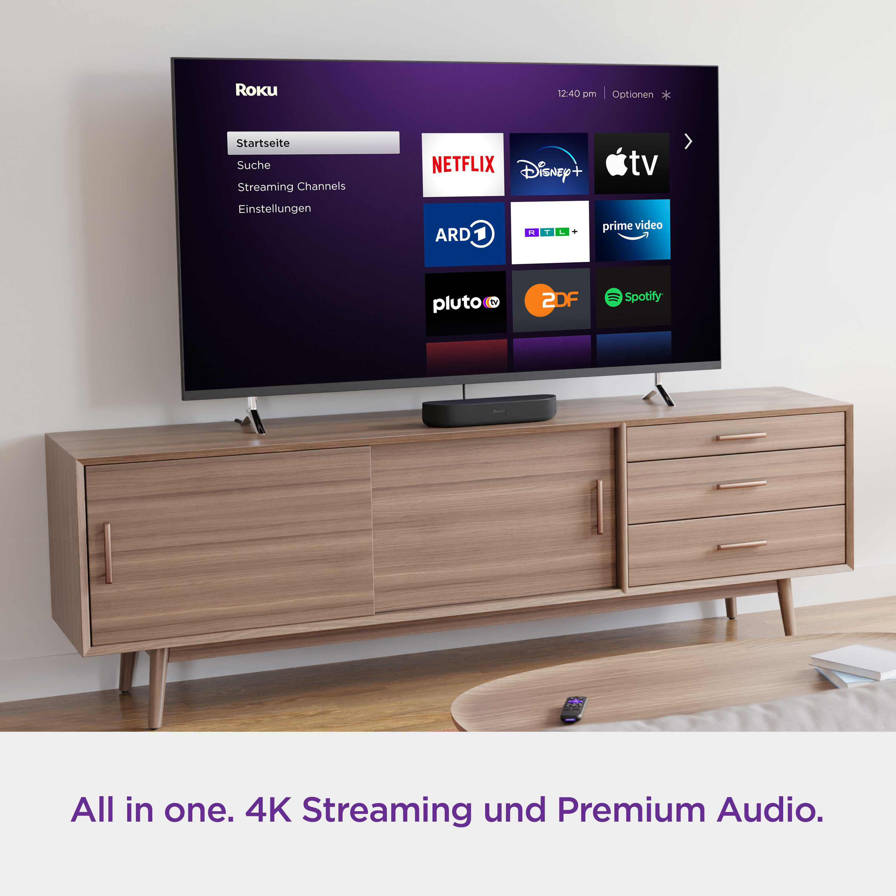 Roku Soundbar unter einem Fernseher auf einem Holzschrank, Fernbedienung auf dem Tisch.