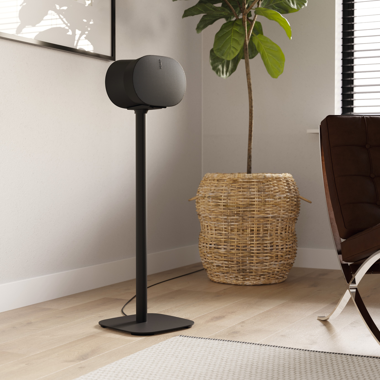 A black speaker on a stand, with a plant in a basket and a brown chair in a well-lit room.