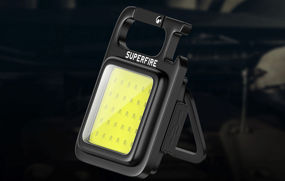 Czarna latarka z karabińczykiem, z jasnym światłem LED i składaną podstawką, zdjęcie produktu na rozmytym tle.