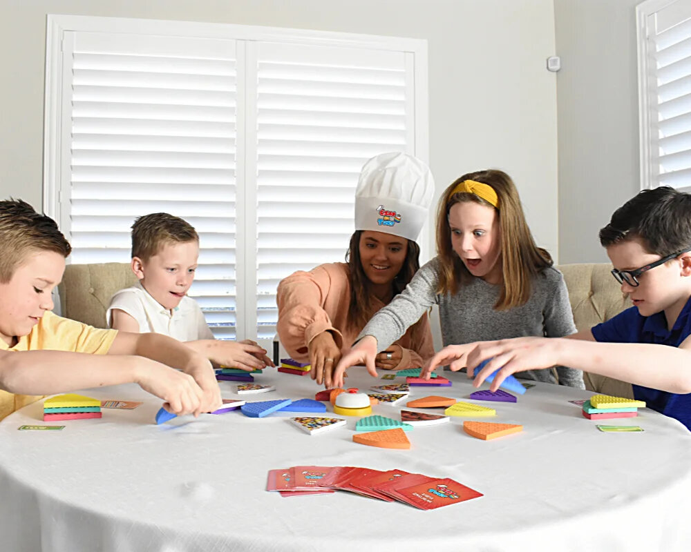 Grupa dzieci grających w grę planszową przy stole z kartami i elementami gry.