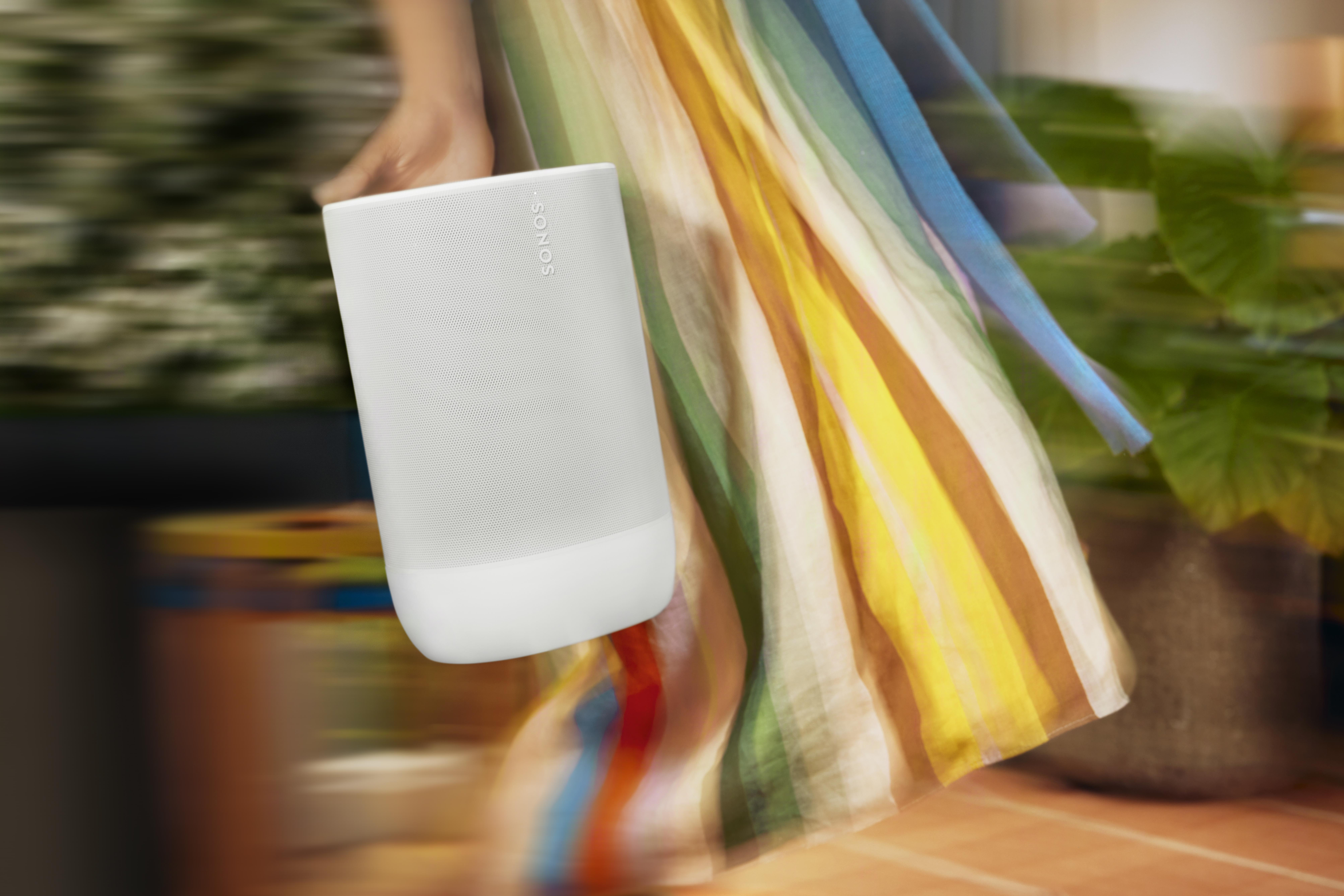Eine Person hält einen weißen Sonos-Lautsprecher, mit Bewegungsunschärfe und einem bunten Kleid im Hintergrund.