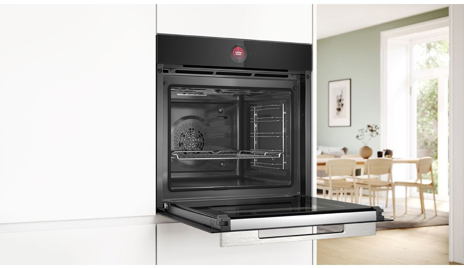 Four ouvert avec grilles intérieures, dans une cuisine blanche. Fenêtre et table en arrière-plan.