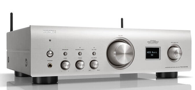 Srebrny odbiornik audio Denon z przyciskami, pokrętłami i wyświetlaczem. Czarne anteny. Białe tło.