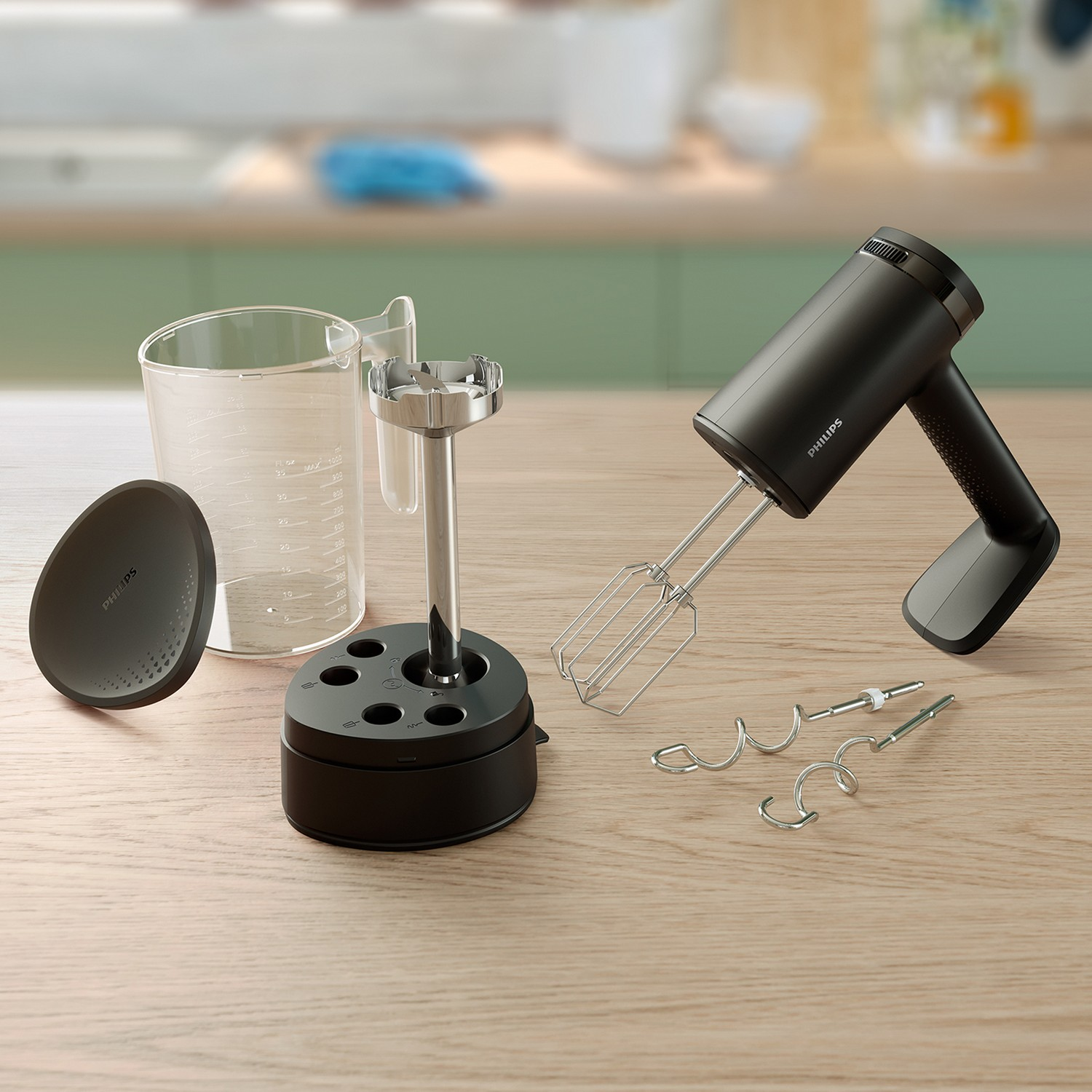 Black hand mixer with attachments and a clear beaker, all on a wooden surface in a kitchen.