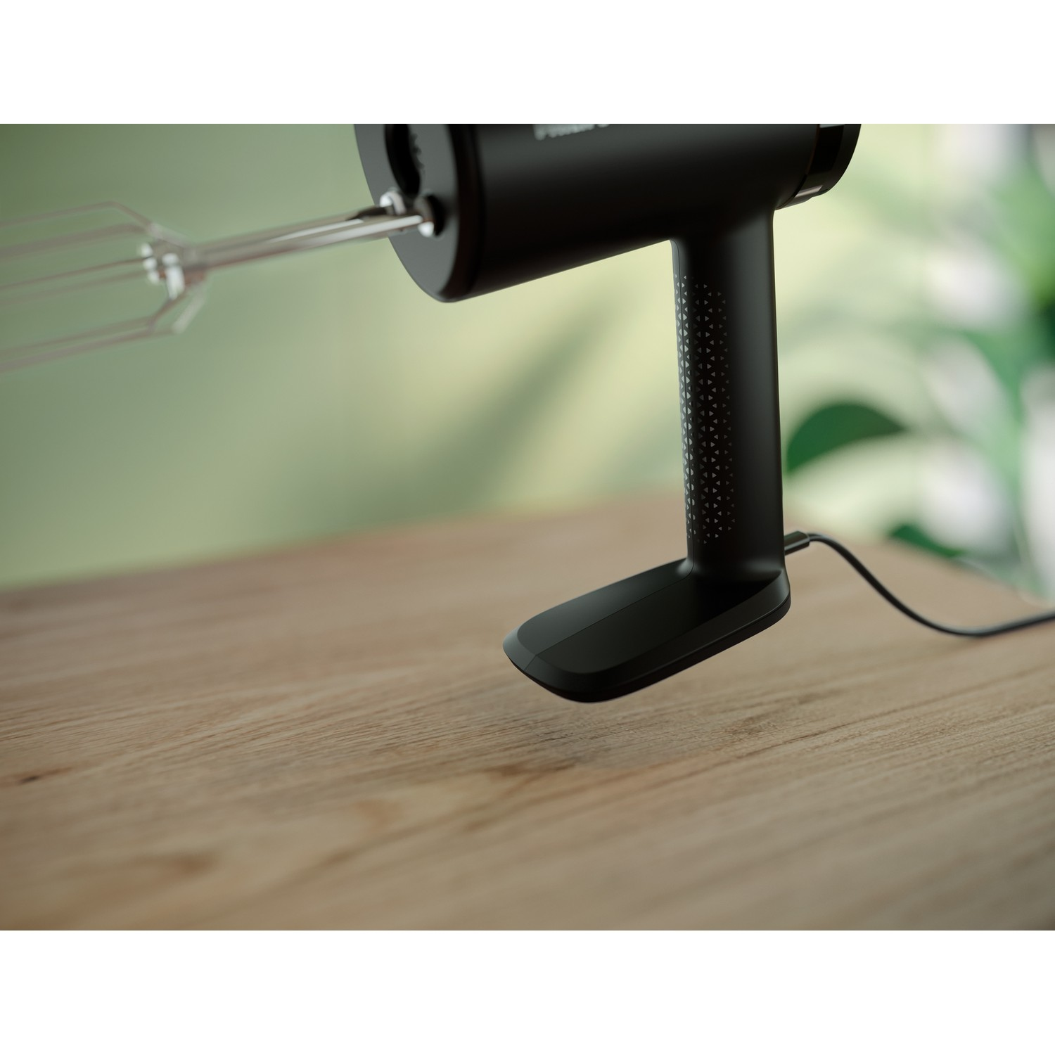 Black hand mixer on a wooden table. A beater is attached to it. Green background.