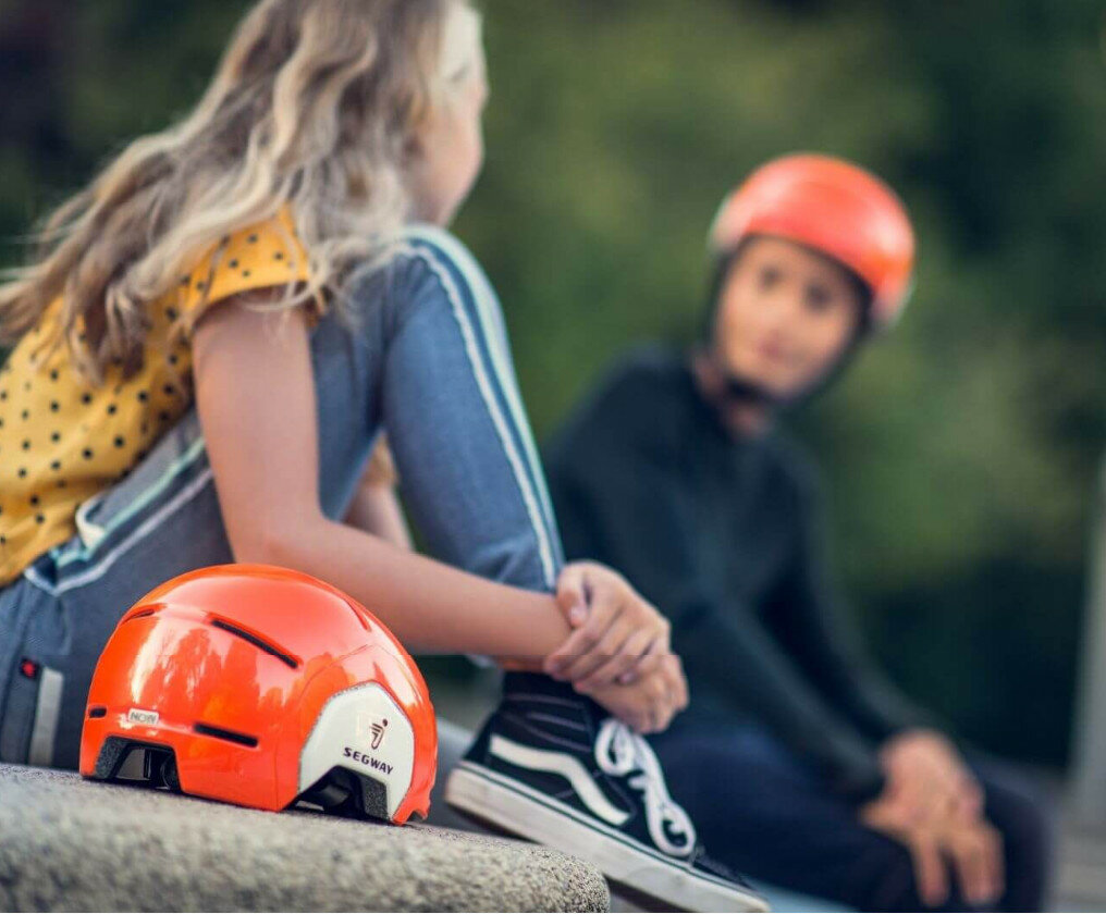 Dwoje dzieci siedzi na zewnątrz, pomarańczowy kask z przodu.