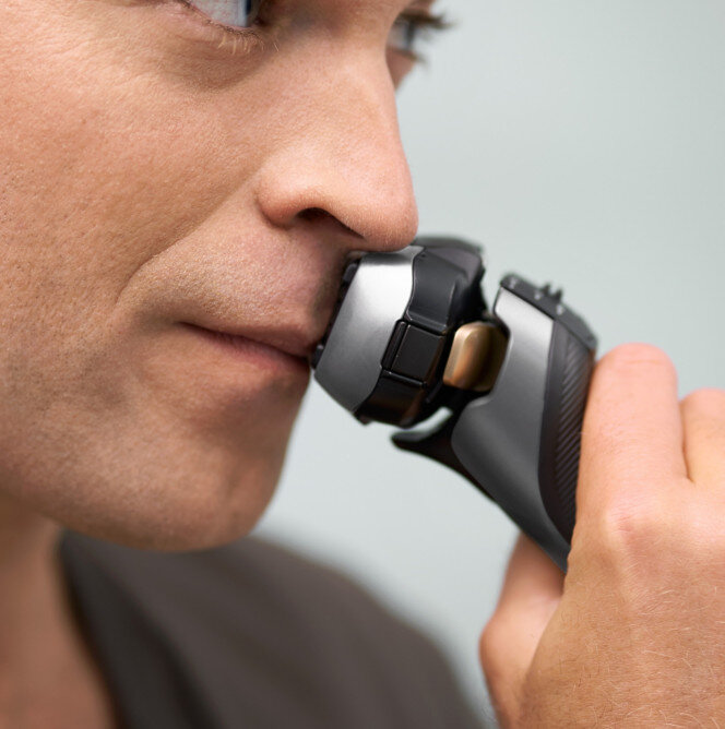 Mężczyzna golący twarz golarką elektryczną.