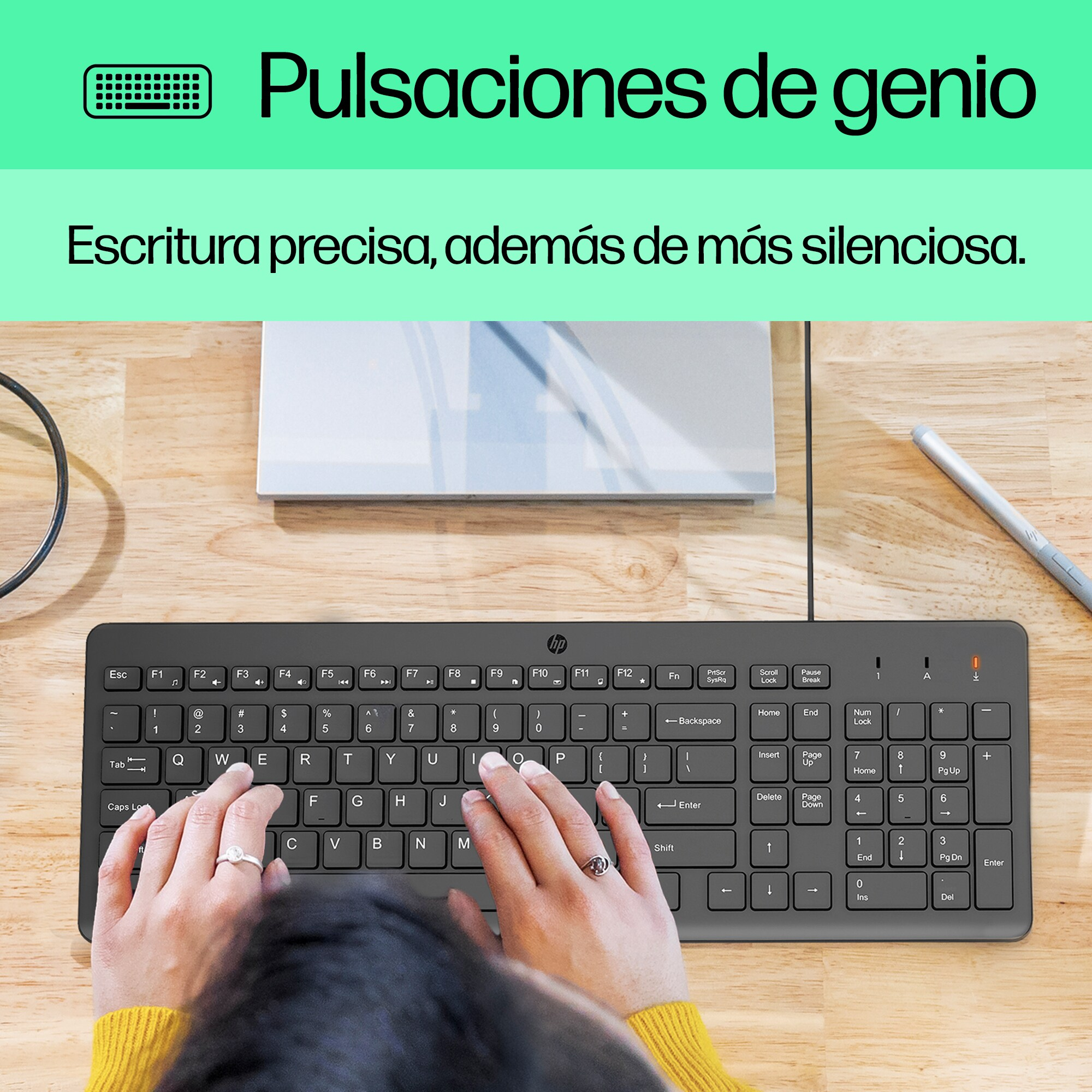 Una persona escribe en un teclado negro sobre un escritorio de madera.