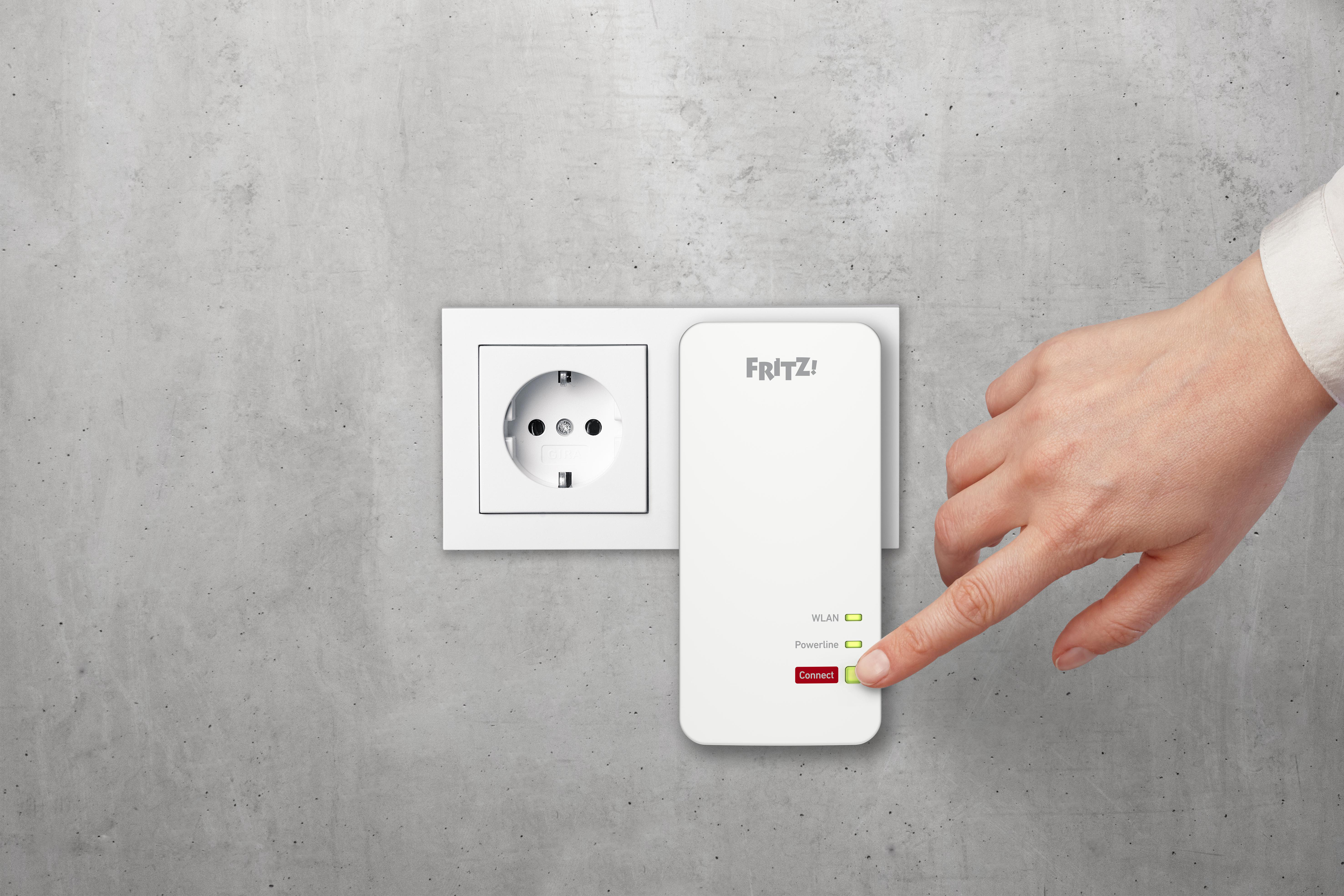Eine Hand drückt die Connect-Taste auf einem weißen Fritz!-Gerät. Das Gerät befindet sich neben einer Steckdose.