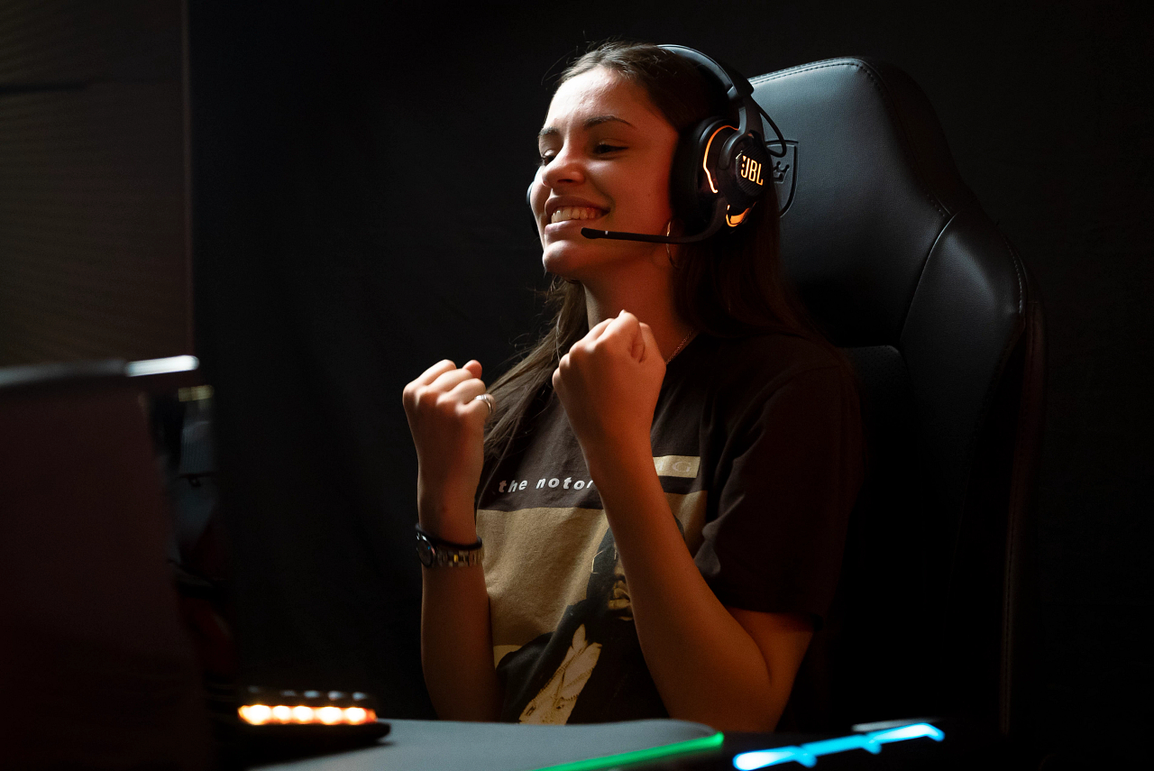 Ein Mädchen mit Headset feiert einen Gaming-Sieg, lächelt und ballt die Fäuste.