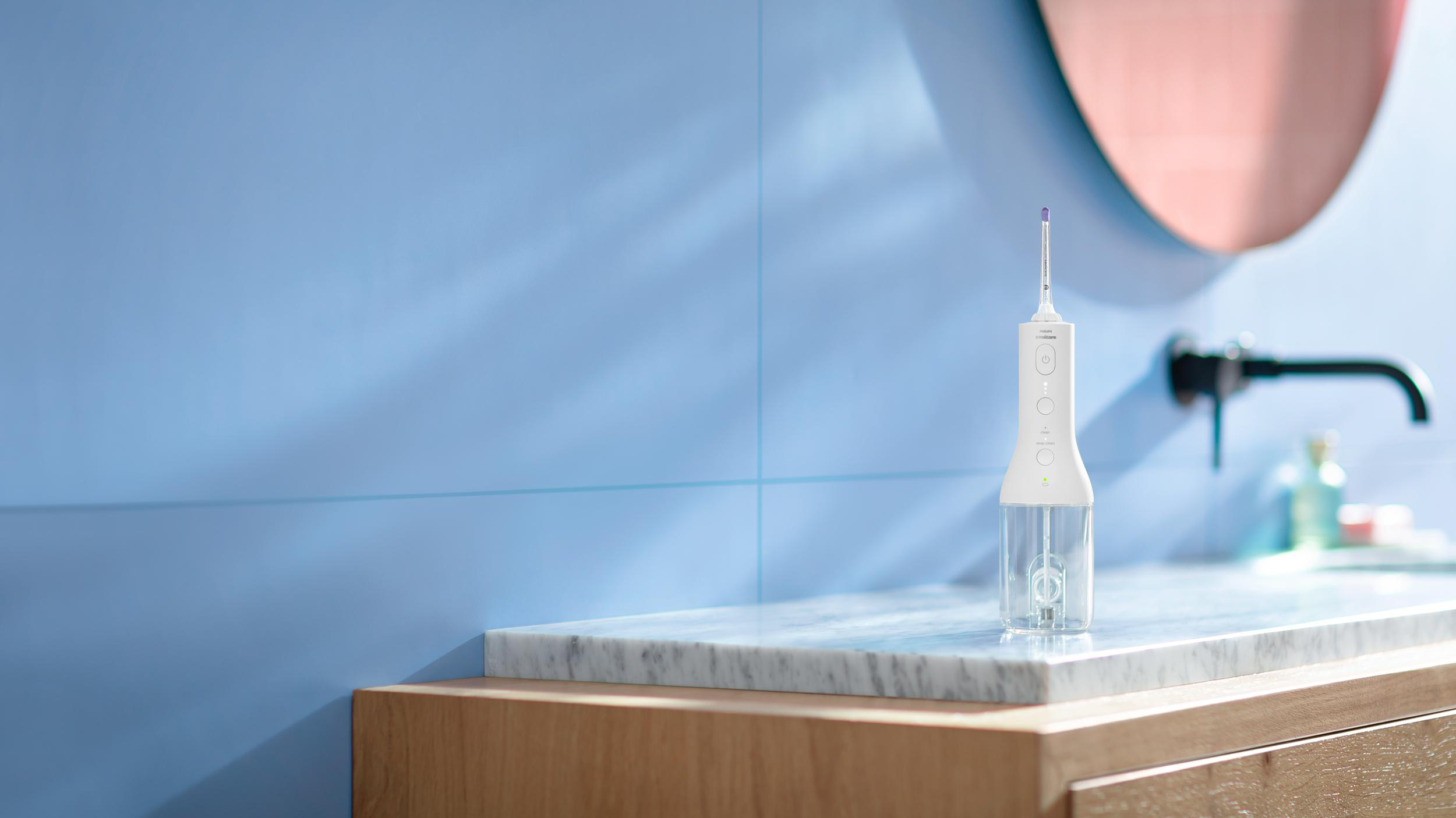 Ein weißer Wasserflosser steht auf einer Marmorarbeitsplatte neben einem Waschbecken und Spiegel.