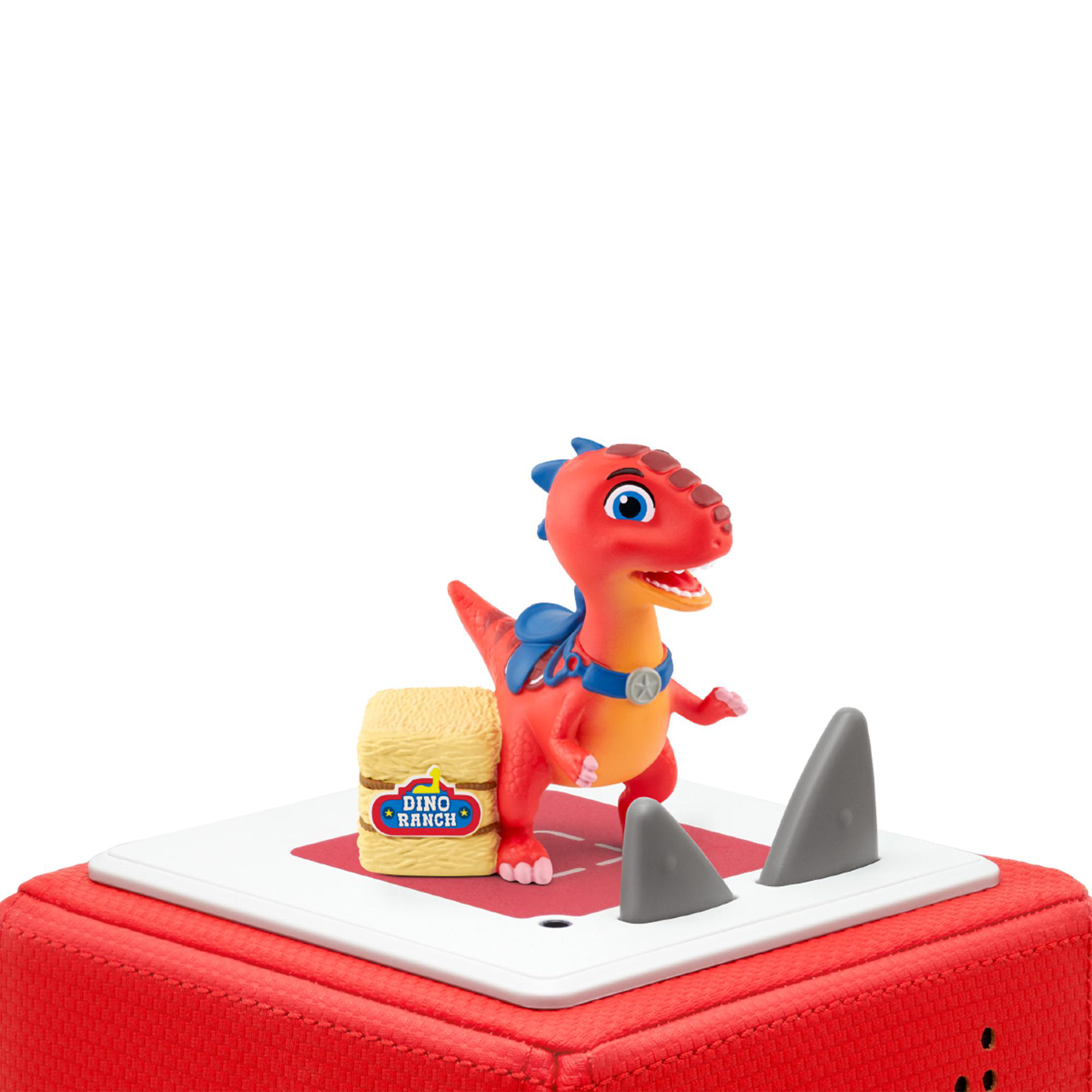 Ein rotes Dinosaurierspielzeug auf einer Plattform. Es hat einen kleinen Heuballen und graue Felsen.