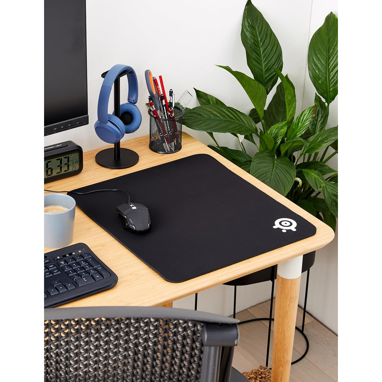 Configurazione scrivania: tappetino nero, cuffie, tastiera e pianta.