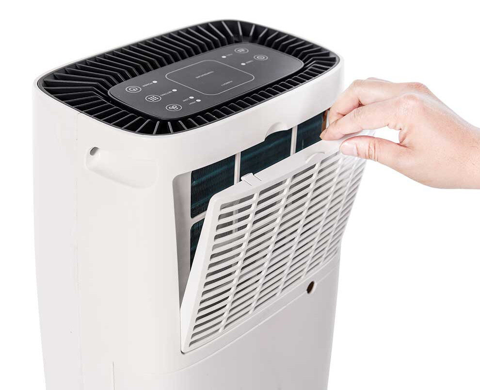 Biały oczyszczacz powietrza z ręką osoby wyjmującą filtr z boku urządzenia.
