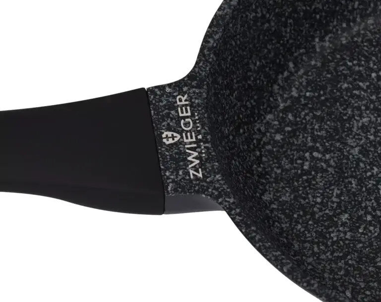 Zbliżenie czarnej i szarej patelni z czarnym uchwytem. Widoczna jest nazwa marki 'ZWIEGER'.